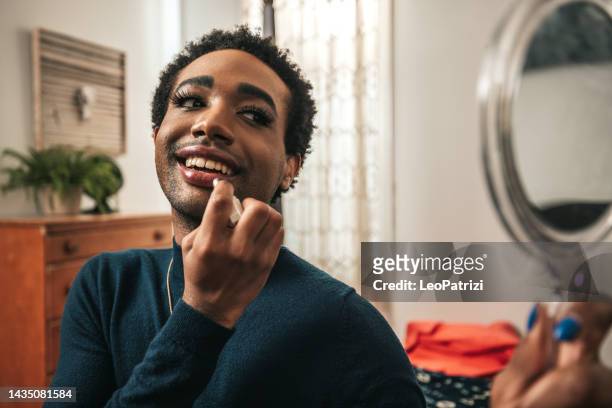 non-binary person making up with lipstick and mascara - black transvestite stock pictures, royalty-free photos & images