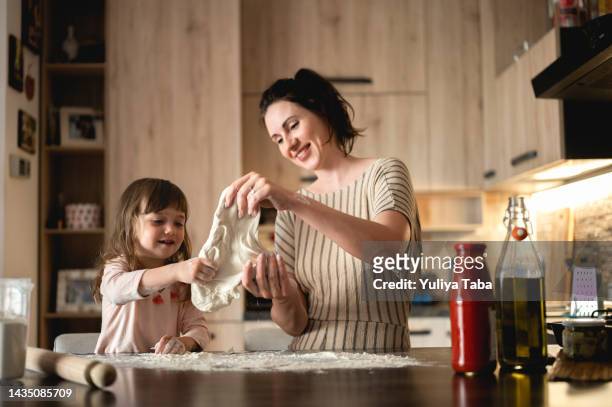 woman with child preparing dough for homemade pizza. mother and children cooking pizza in kitchen. - knåda bildbanksfoton och bilder