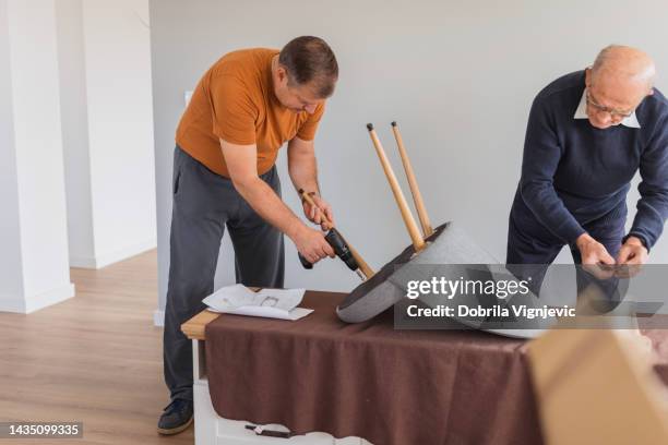 senior man assisting his son using a drill when assembling a chair - restoring chair stock pictures, royalty-free photos & images