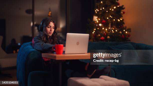 junge frau, die sich zu hause entspannt und zu weihnachten den laptop im wohnzimmer benutzt - büro bäume nacht stock-fotos und bilder