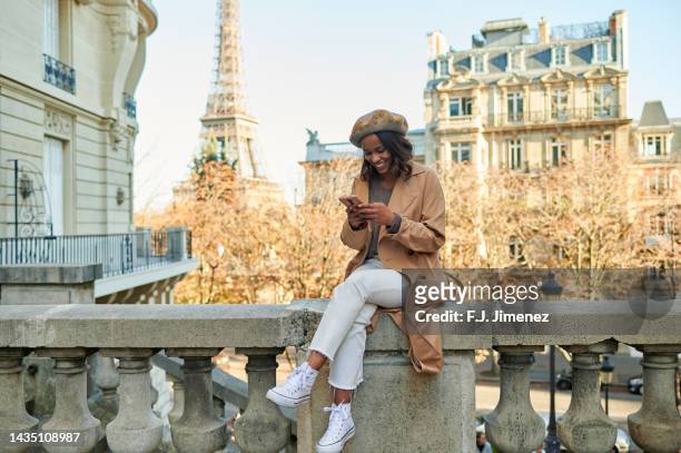 woman using mobile phone in the street of paris with the eiffel tower in the background - paris street stock-fotos und bilder