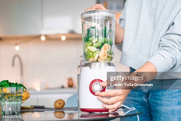 a young woman whips fruits and vegetables in a blender to make a smoothie. - blended drink ストックフォトと画像