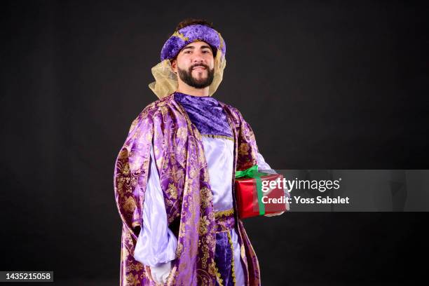 young man disguised as an arab with gift box looking at camera - king royal person stock-fotos und bilder