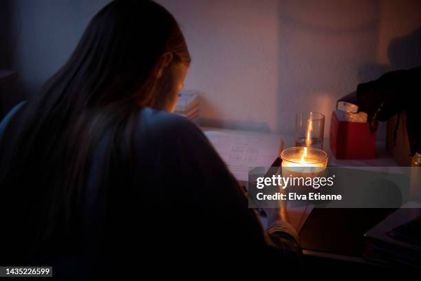 teenager doing homework at a desk by candlelight during an electrical power cut. - corte de luz fotografías e imágenes de stock