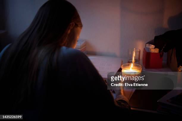 teenager doing homework at a desk by candlelight during an electrical power cut. - blackout stock pictures, royalty-free photos & images