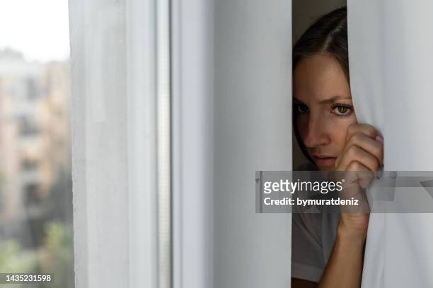 woman scared looking through the window seeking safety - attacking stockfoto's en -beelden