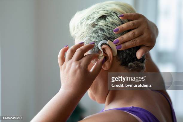 frau legt hörgerät auf ihr ohr - hearing loss stock-fotos und bilder