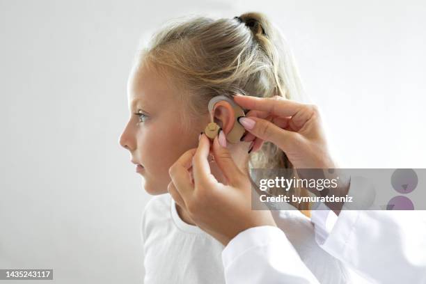 arzt legt ein hörgerät in das ohr eines kindes - audiologist stock-fotos und bilder