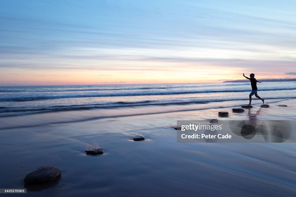 Boy walking on stepping stones at sunset