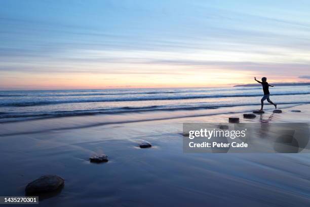 boy walking on stepping stones at sunset - stappen stockfoto's en -beelden