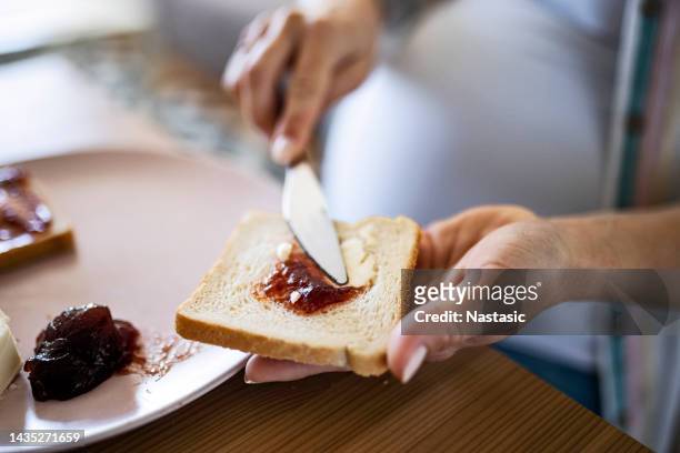 unrecognizable young pregnant woman alone in her kitchen enjoying a breakfast - marmalade sandwich stock pictures, royalty-free photos & images