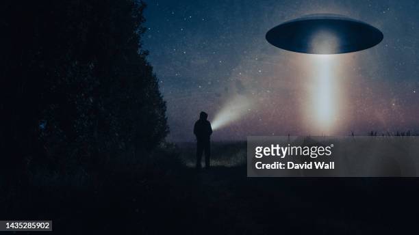 a science fiction concept of a man with a torch looking at an alien ufo. floating above a field on a spooky foggy night in the countryside. - flying saucer fotografías e imágenes de stock