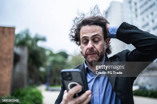 hombre de negocios maduro preocupado usando el teléfono móvil en la calle - sin esperanza fotografías e imágenes de stock