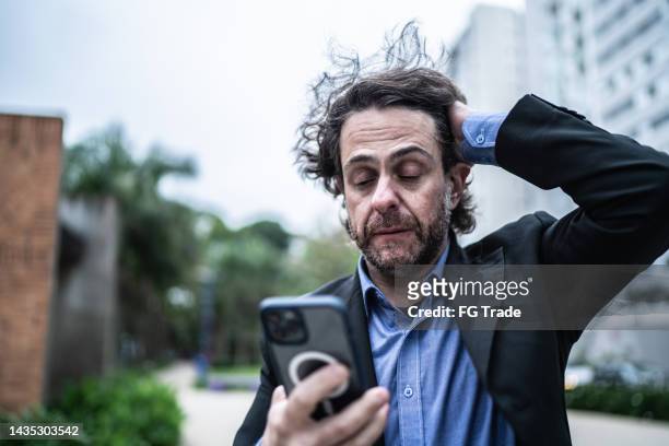 worried mature businessman using the mobile phone in the street - distressed stock market people stock pictures, royalty-free photos & images