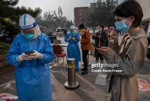 An epidemic control worker registers a woman for a nucleic acid test to detect COVID-19 as journalists, staff, and officials line up for test outside...