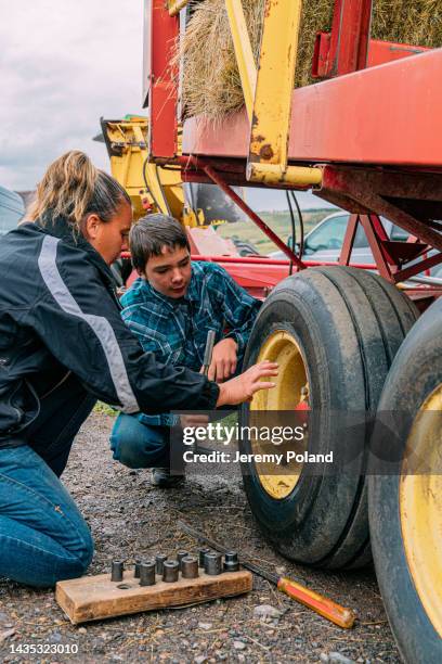 middle-aged caucasian mother explaining to her young teenage son how to change a tire on a bale wagon for accumulating, stacking, and moving hay or straw on a small town family-owned ranch in colorado, usa - agricultural equipment stock pictures, royalty-free photos & images