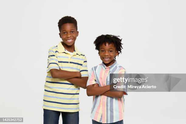 portrait of two young african american generation z boys smiling and standing with the arms crossed. both wearing a striped shirt in a studio setting. - kids standing crossed arms stock-fotos und bilder