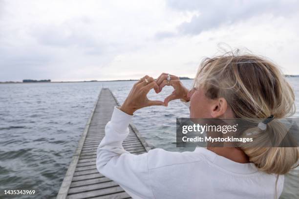 happy woman on wooden pier makes a heart shape finger frame with hands - denmark landscape stock pictures, royalty-free photos & images