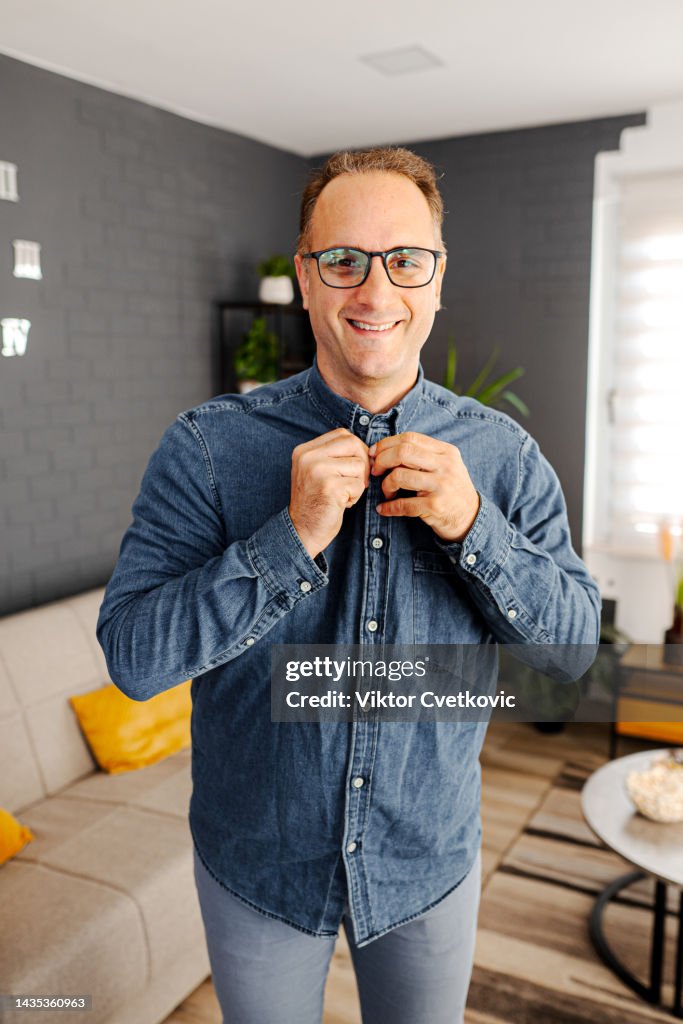 Portrait of an handsome white man buttoning down his shirt in the living room
