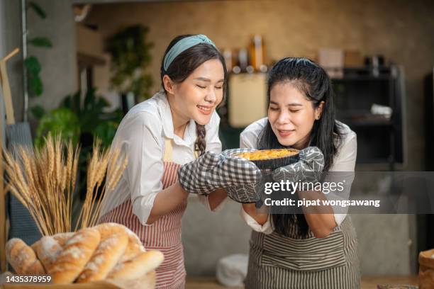 two girlfriends are picking up freshly made pies and smell them proud of their craftsmanship. - smelling food stock pictures, royalty-free photos & images