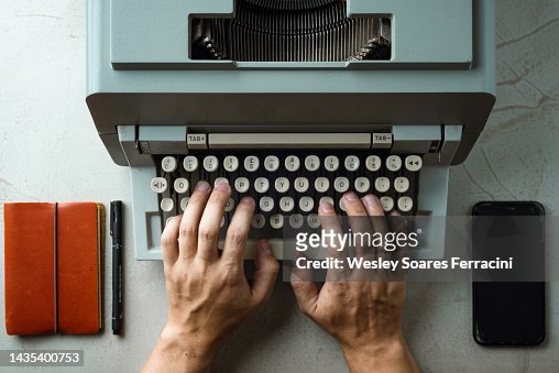 Flat lay image of human man hands typing old typewriter on a business office desk with leather notepad and cellphone