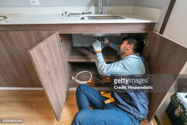 plumber fixing a leak in the kitchen sink of a house - broken pipe stockfoto's en -beelden