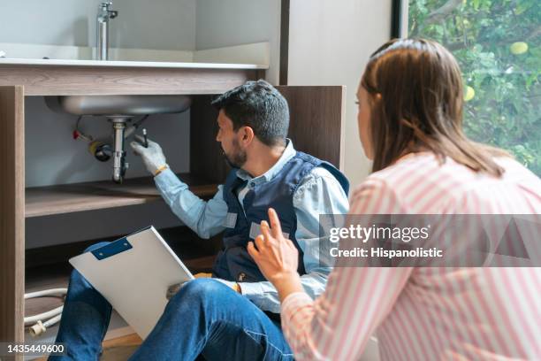 plumber explaining to a client the problem with her kitchen sink - repareren stockfoto's en -beelden