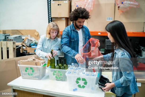 diverse group of volunteers at a recycling centre separating glass, cardboard and plastic in to different containers - circulaire economie stockfoto's en -beelden