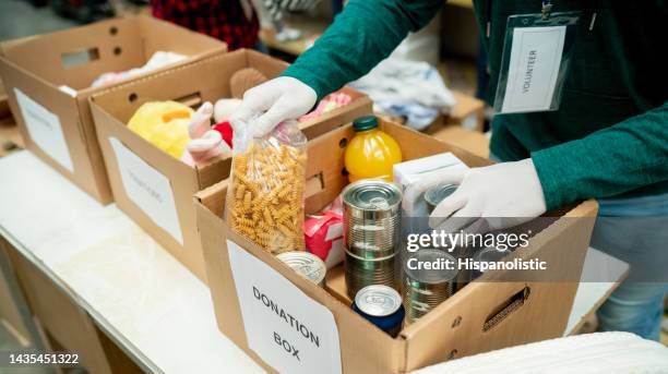 unrecognizable volunteer organizing donations in boxes wearing protective gloves - liefdadigheidsinstelling stockfoto's en -beelden