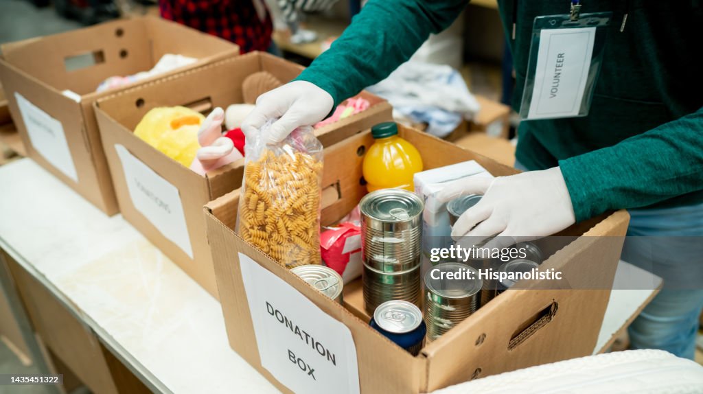 Unrecognizable volunteer organizing donations in boxes wearing protective gloves