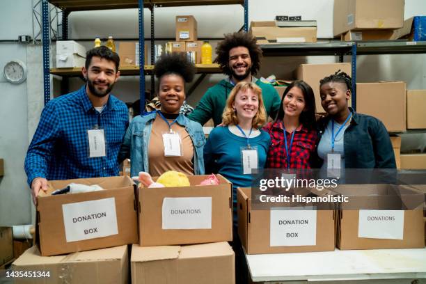 large group of diverse volunteers at a charitable foundation standing behind a table with donation boxes facing camera smiling - charitable foundation stockfoto's en -beelden