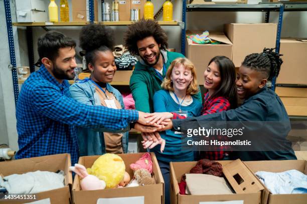 diverse group of volunteers receiving and organizing donations in boxes all with hands in a huddle - relief emotion stock pictures, royalty-free photos & images