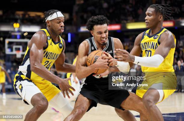 Tre Jones of the San Antonio Spurs is defended by Buddy Hield and Bennedict Mathurin of the Indiana Pacers at Gainbridge Fieldhouse on October 21,...