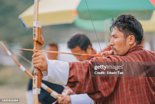 bhutanese man practicing archery aiming and shooting  in field - bhutan archery stock pictures, royalty-free photos & images