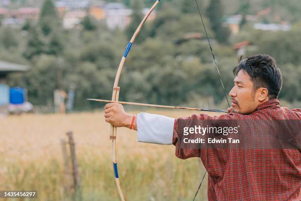 bhutanese man practicing archery aiming and shooting  in field - bhutan archery stock pictures, royalty-free photos & images
