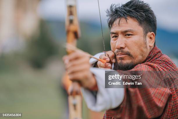 bhutanesischer mann übt bogenschießen und schießen im feld - longbow stock-fotos und bilder