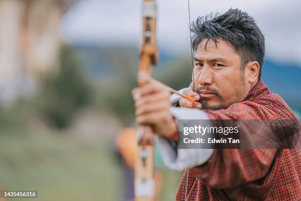 uomo bhutanese che pratica il tiro con l'arco mira e tiro sul campo - arco da guerra foto e immagini stock