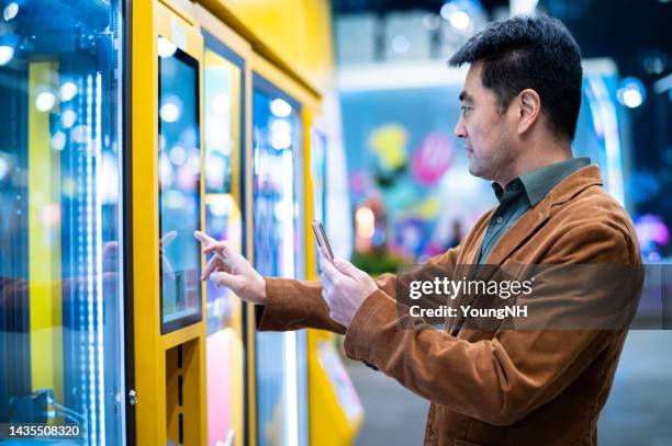 asian middle-aged man shopping in vending machine - verkoopautomaat stockfoto's en -beelden