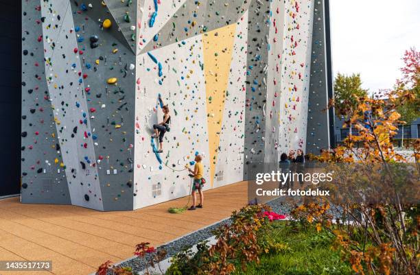 woman doing rock climbing on artificial climbing wall with instructor standing below - sport climbing stock pictures, royalty-free photos & images