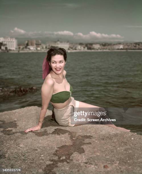 Yvonne De Carlo wearing green bikini top and shorts posing on sea wall circa 1948.