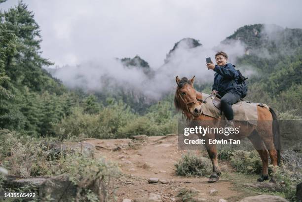 asian chinese female tourist riding horse prepare hiking up to taktsang monastery , tiger nest in bhutan - disparo bildbanksfoton och bilder