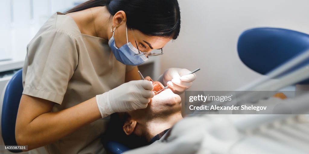 Ritratto di gruppo di due persone, donna dentista che fa il trattamento nella clinica moderna per l'uomo. Fotografia di concept medicale al chiuso per odontoiatria. Studio dentistico, medico che lavora in clinica con il paziente.