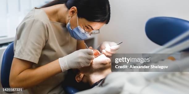 group portrait of two people, woman dentist making treatment in modern clinic for man. medical concept photography indoors for dentistry. dental office, doctor working in clinic with patient. - dental health imagens e fotografias de stock