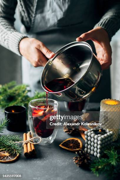 woman in gray warm sweater and apron pouring hot mulled wine in a glass. concept of winter season drink - glühwein stock-fotos und bilder