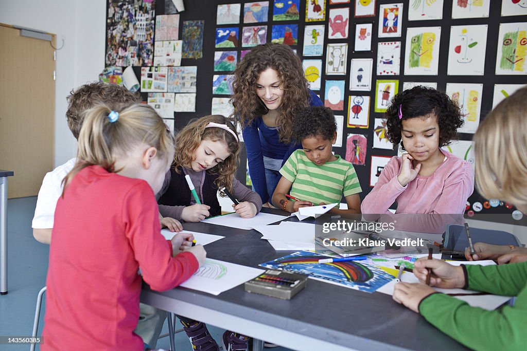 Teacher together with kids drawing in classroom