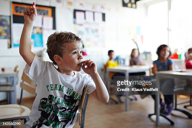 cute boy with raised hand in classroom - élève du primaire photos et images de collection