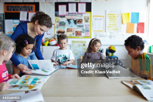 Teacher looking in books with children Teacher looking in books with children