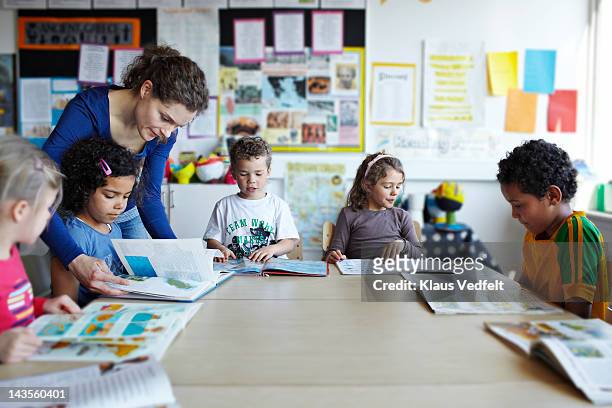 teacher looking in books with children - education stock pictures, royalty-free photos & images