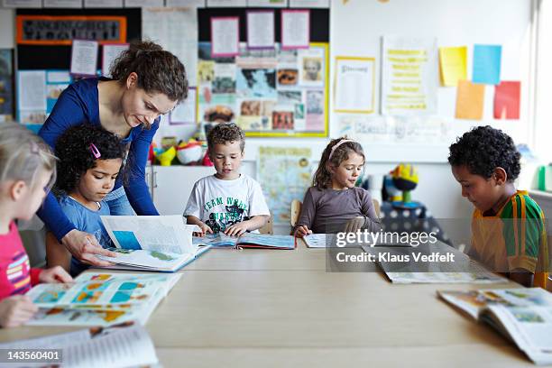 teacher looking in books with children - elementary age stock pictures, royalty-free photos & images
