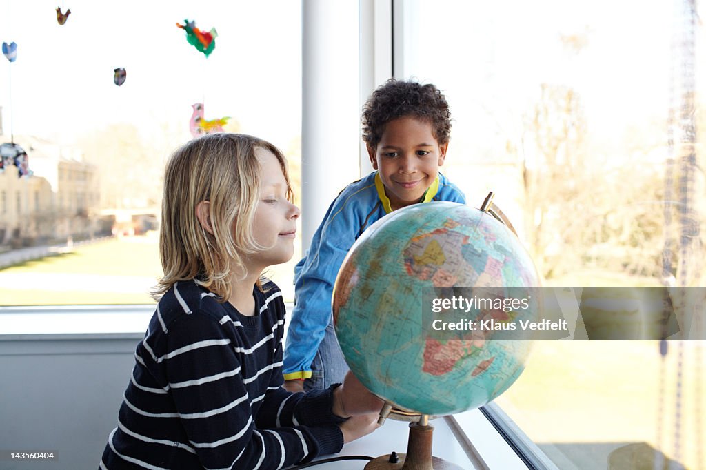 2 boys smiling,  looking at globe